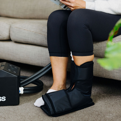 Woman sitting on a couch with a plant and a coffee cup, using a black compression device labeled 'Isopress'.