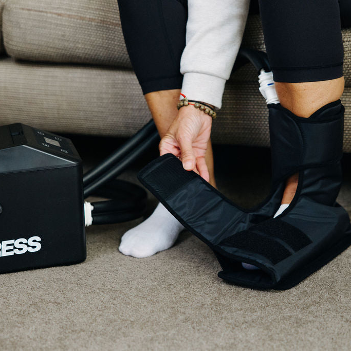 Woman sitting on a couch using a black Ankle cryocuff
