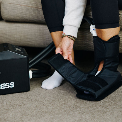 Woman sitting on a couch using a black Ankle cryocuff