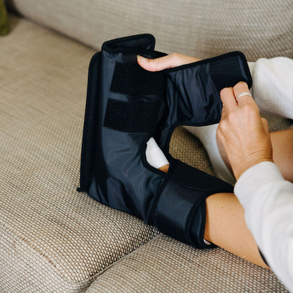 Woman sitting on a couch using a black compression device
