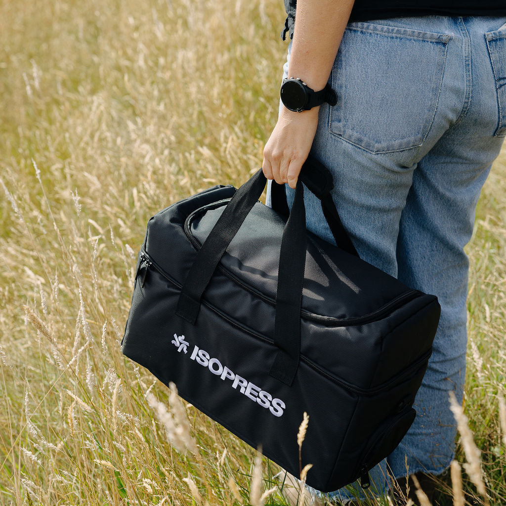 Person holding a black bag with Isopress logo in a grassy field