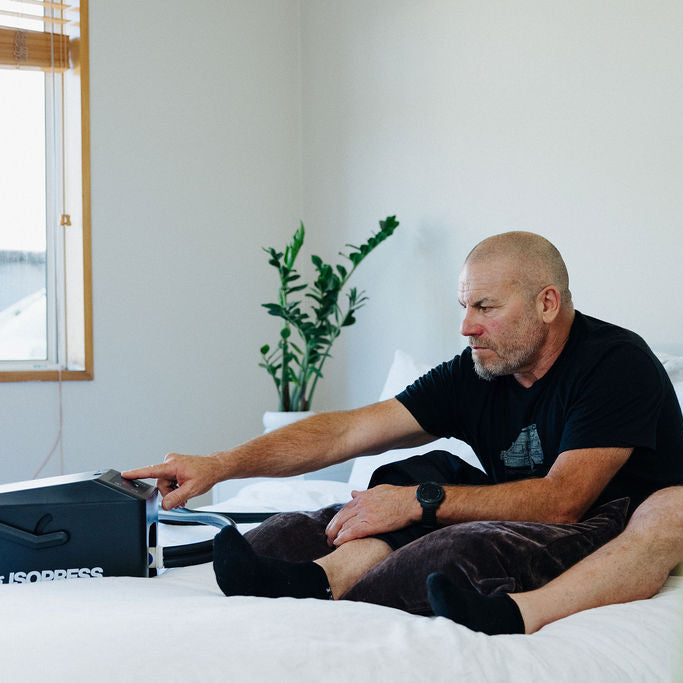 Man sitting on a bed using an Isopress with a plant and window in the background