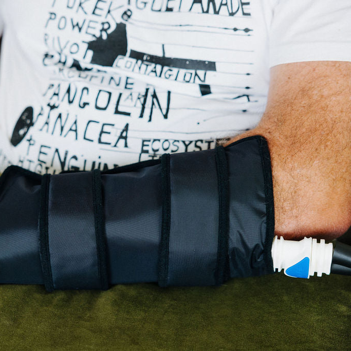 Person using an ice cryocuff on their wrist while sitting on a couch.