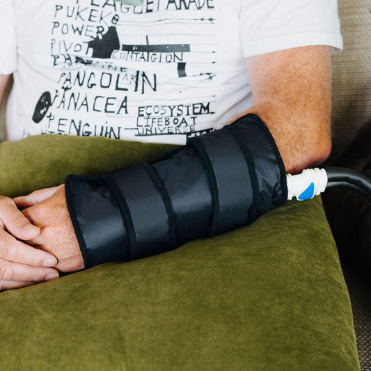 Person using an ice cryocuff on their wrist while sitting on a couch.