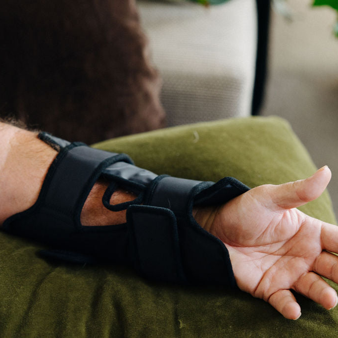 Person using an ice cryocuff on their wrist while sitting on a couch.